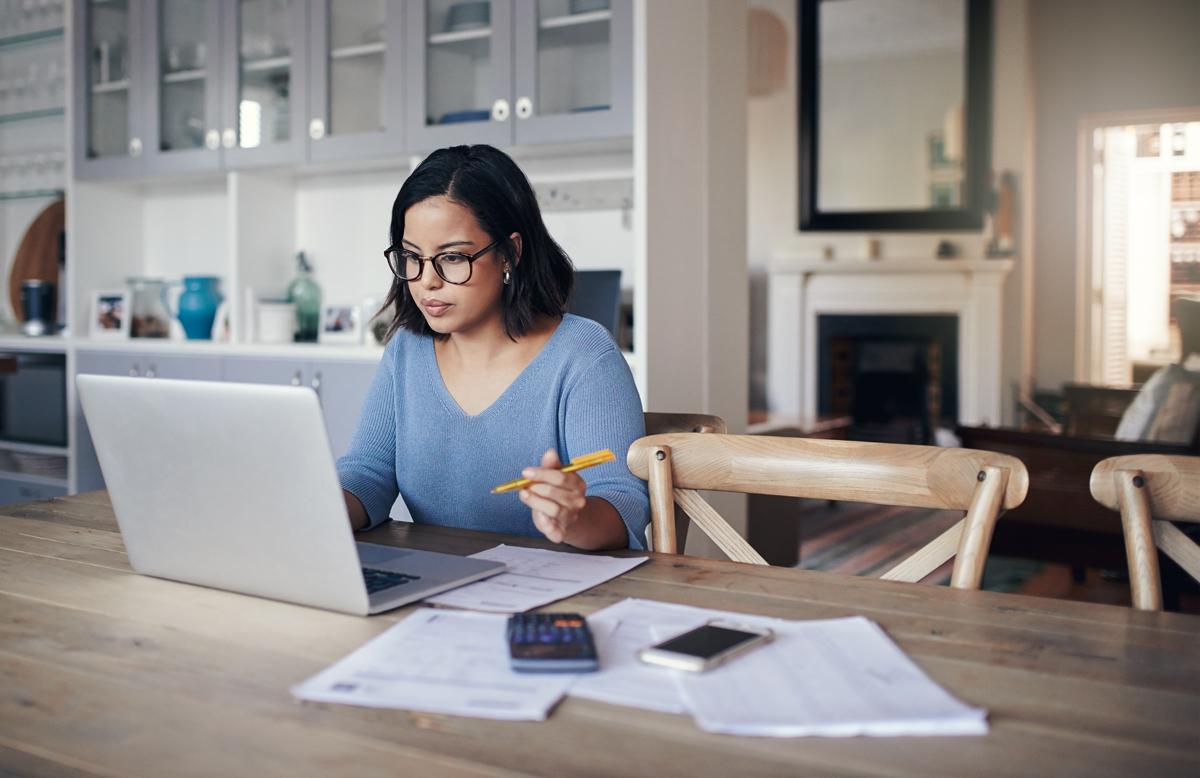 Woman working out her finances on her laptop in the kitchen.